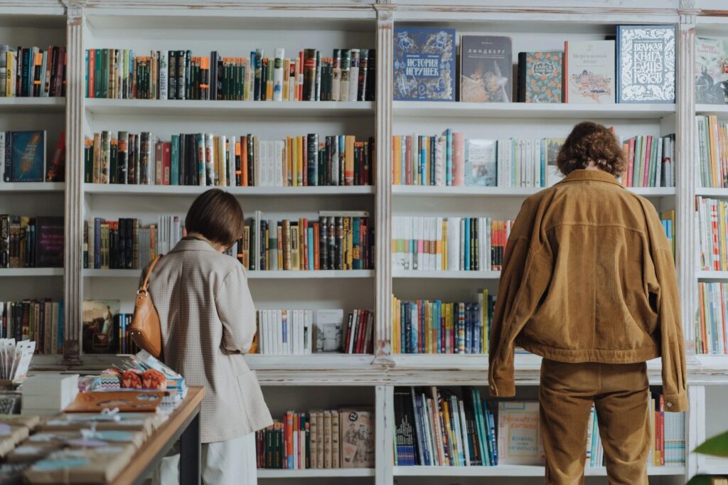 Two adults stand with their backs turned to the camera in front of bookcases full of brightly colored books