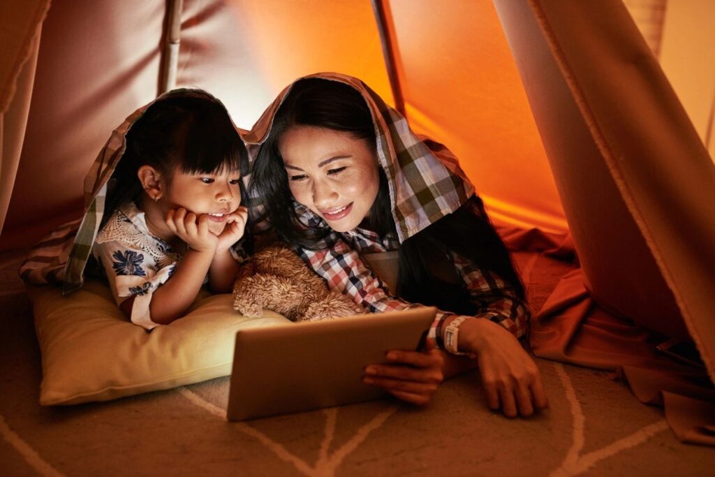 An adult and child look at a tablet screen together in a tent