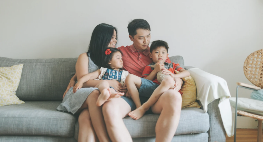 2 adults sit on a light blue couch, cuddling their 2 kids